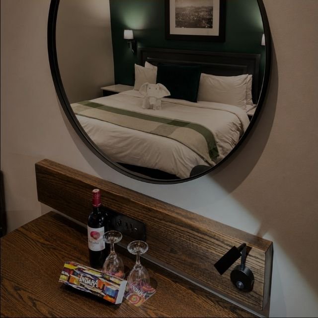 A bottle of red wine, two glasses, and welcome treats reflected in a round wall mirror above the desk at Indaba Hotel Spa and Conference Centre in Johannesburg.