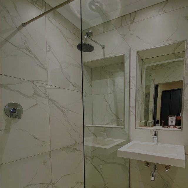 A contemporary white marble-tiled bathroom featuring a glass walk-in rain shower and vanity sink at Indaba Hotel Spa and Conference Centre in Johannesburg.