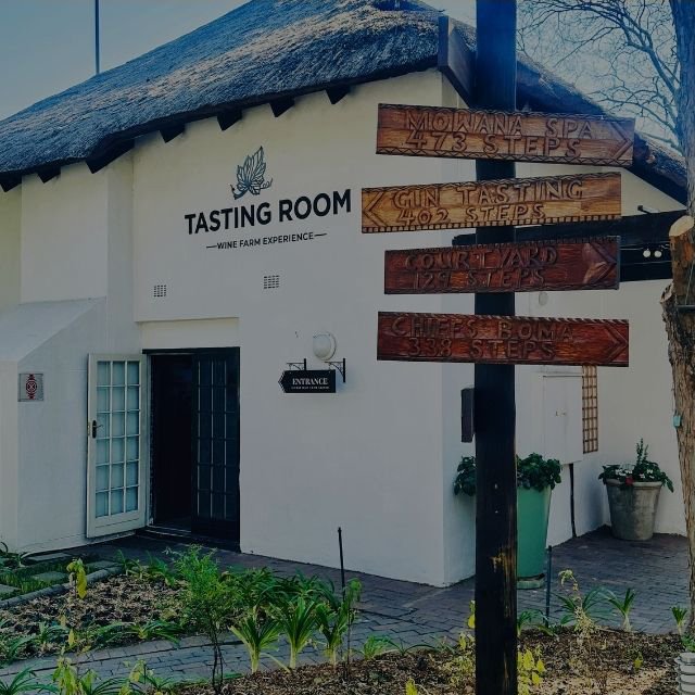 The white exterior facade of the Tasting Room featuring directional wooden signs pointing toward the spa, gin tasting, and courtyard at Indaba Hotel Spa and Conference Centre in Johannesburg.