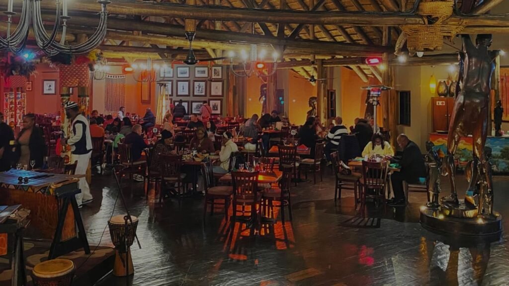 A warm, vibrant interior of the restaurant dining hall featuring wooden beams, African-inspired decor, and guests dining at tables at Indaba Hotel Spa and Conference Centre in Johannesburg.