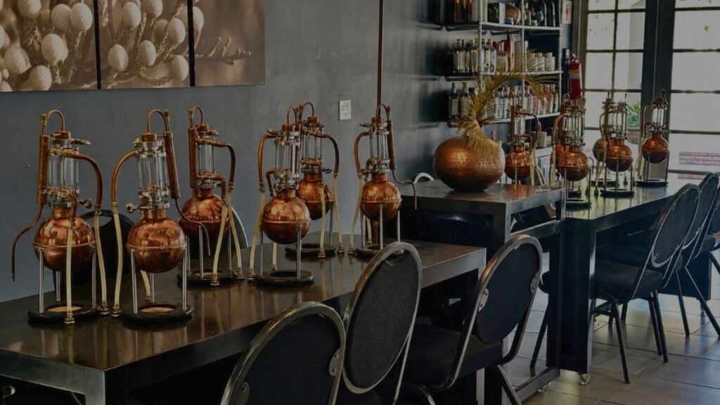 A row of copper gin distillation apparatuses set up on dark wooden tables inside the Gin School at Indaba Hotel Spa and Conference Centre in Johannesburg.