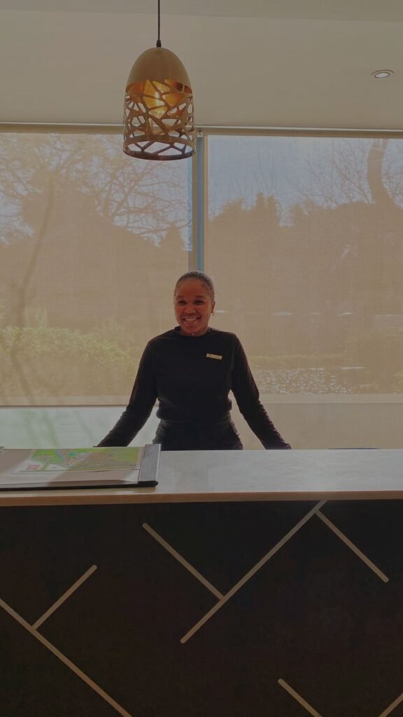 A smiling staff member welcoming guests at the front desk of Indaba Hotel Spa and Conference Centre in Johannesburg.