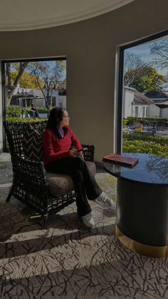 Claudia Sherrin relaxing in a black wicker chair in the sunlit lounge overlooking the courtyard at Indaba Hotel Spa and Conference Centre in Johannesburg.