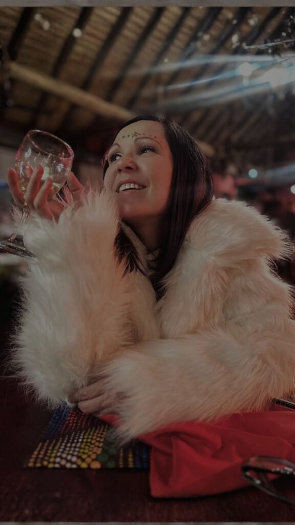 Claudia Sherrin wearing a fluffy white jacket and holding a glass of white wine indoors at Indaba Hotel Spa and Conference Centre in Johannesburg.