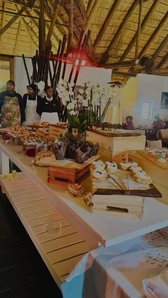 A bountiful buffet table featuring freshly baked pastries, cakes, and desserts with staff members standing in the background at Indaba Hotel Spa and Conference Centre in Johannesburg.