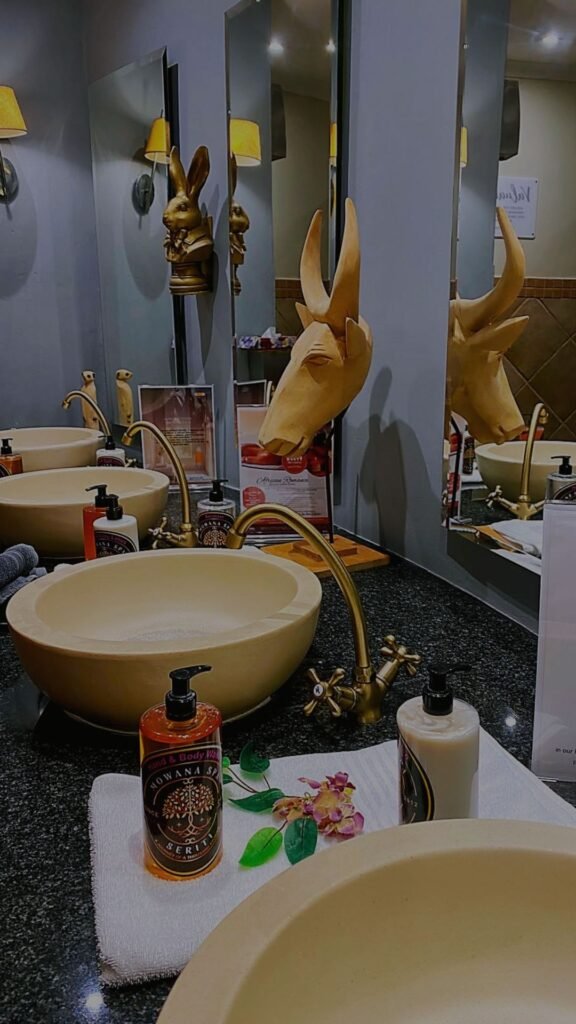 Elegant stone basin sinks, brass faucets, and African-themed sculptures on a granite countertop inside the spa restroom at Indaba Hotel Spa and Conference Centre in Johannesburg.