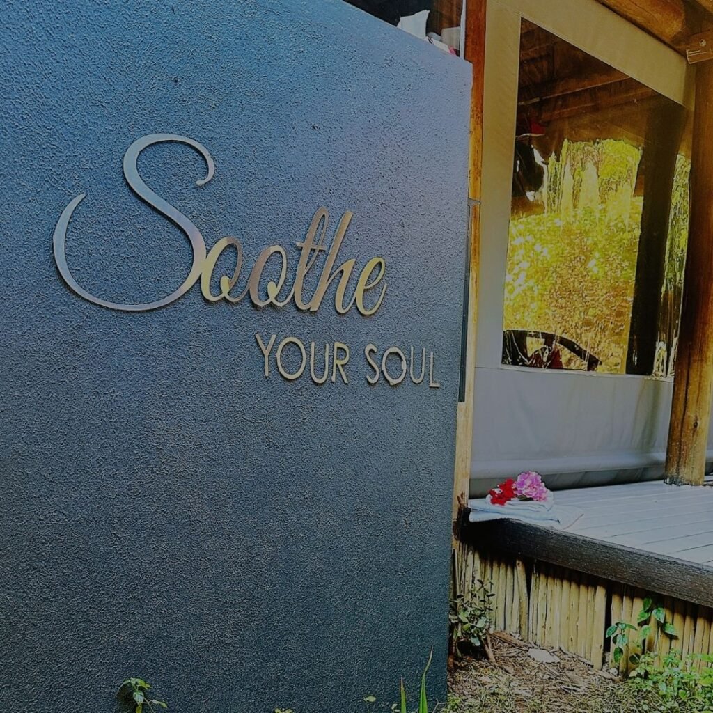 A dark textured exterior wall featuring the metallic inscription "Soothe Your Soul" next to a wooden deck at Indaba Hotel Spa and Conference Centre in Johannesburg.
