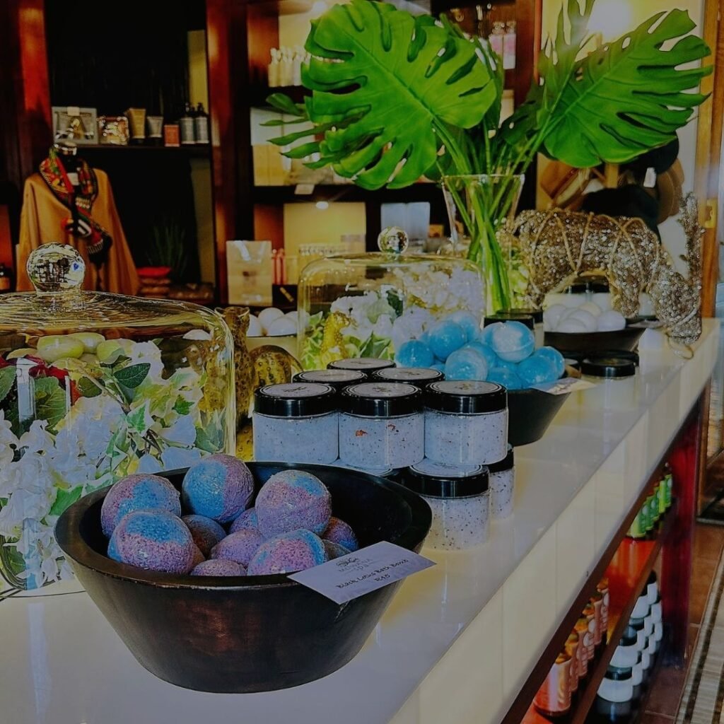 A retail display counter featuring colorful bath bombs in wooden bowls, body scrubs in jars, and decorative tropical greenery at Indaba Hotel Spa and Conference Centre in Johannesburg.