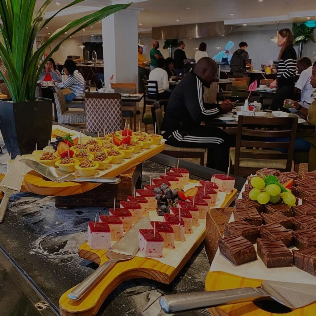 A colorful buffet display of bite-sized desserts including tarts, square cakes, and chocolate brownies on wooden boards at Indaba Hotel Spa and Conference Centre in Johannesburg.