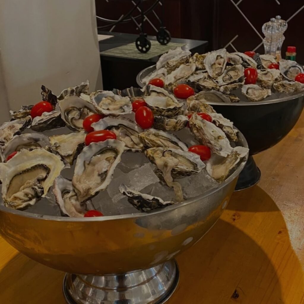 Large bowls filled with crushed ice, freshly shucked oysters, and cherry tomatoes on a wooden table at Indaba Hotel Spa and Conference Centre in Johannesburg.