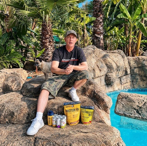Judd sitting poolside with Sport Rx Protein RX, Electrolyte RX and Protein WTR cans, pug in the background