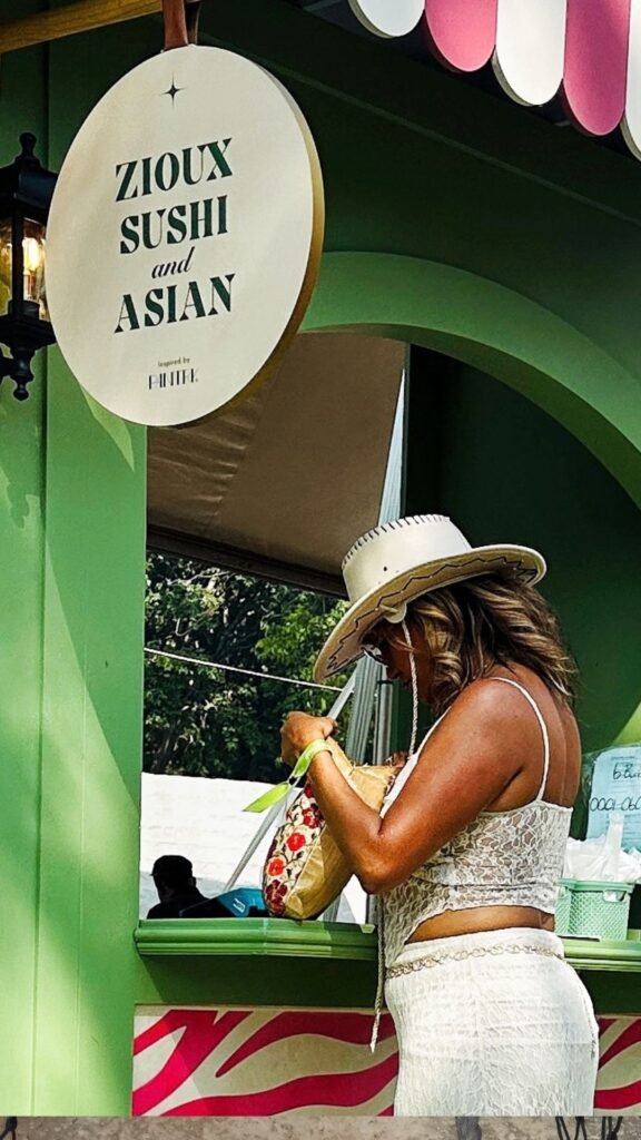 A festival guest ordering food beneath the Zioux Sushi and Asian sign at the culinary playground during the Luxurious Marble Circus.