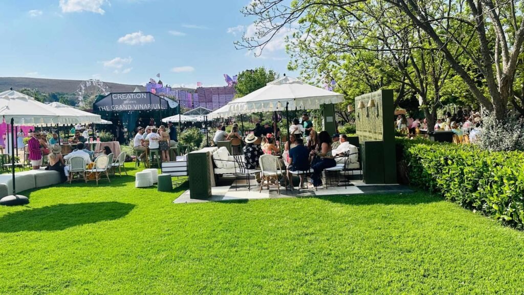Guests relaxing under white umbrellas on the green lawns at the Luxurious Marble Circus festival grounds.