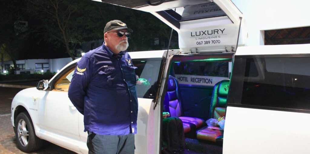 Chauffeur Jaco in Luxury Limousines uniform standing beside the white Porsche Cayenne stretch limousine at night
