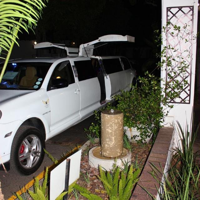 White Porsche Cayenne stretch limousine parked at night with both wing doors raised, showing the full length of the vehicle