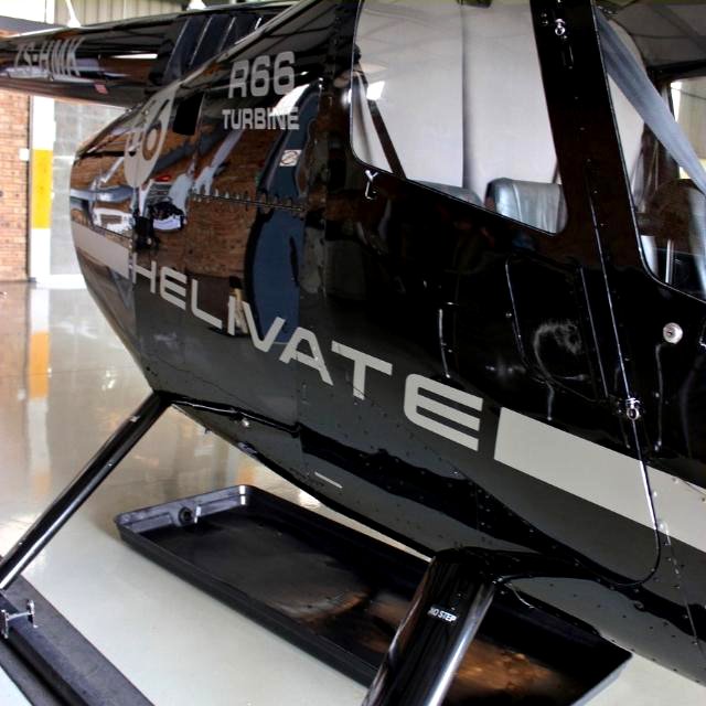 Close-up of the glossy black Helivate R66 Turbine helicopter showing the white HELIVATE lettering and R66 TURBINE marking inside the hangar.