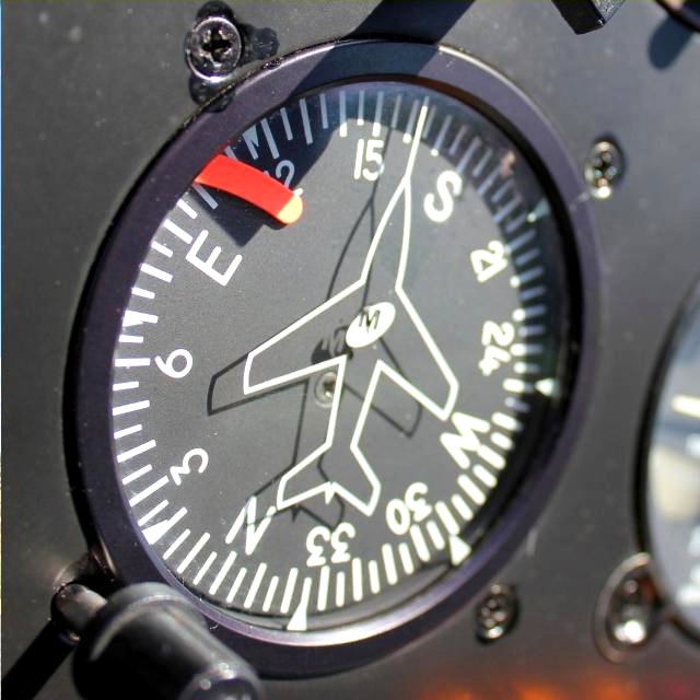 Close-up of the magnetic compass instrument inside a Helivate helicopter cockpit showing the aircraft symbol and directional markings.