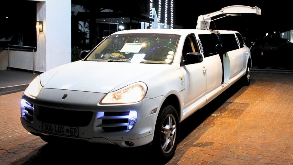 Front three-quarter view of the white Porsche Cayenne stretch limousine with headlights on and wing door open at night