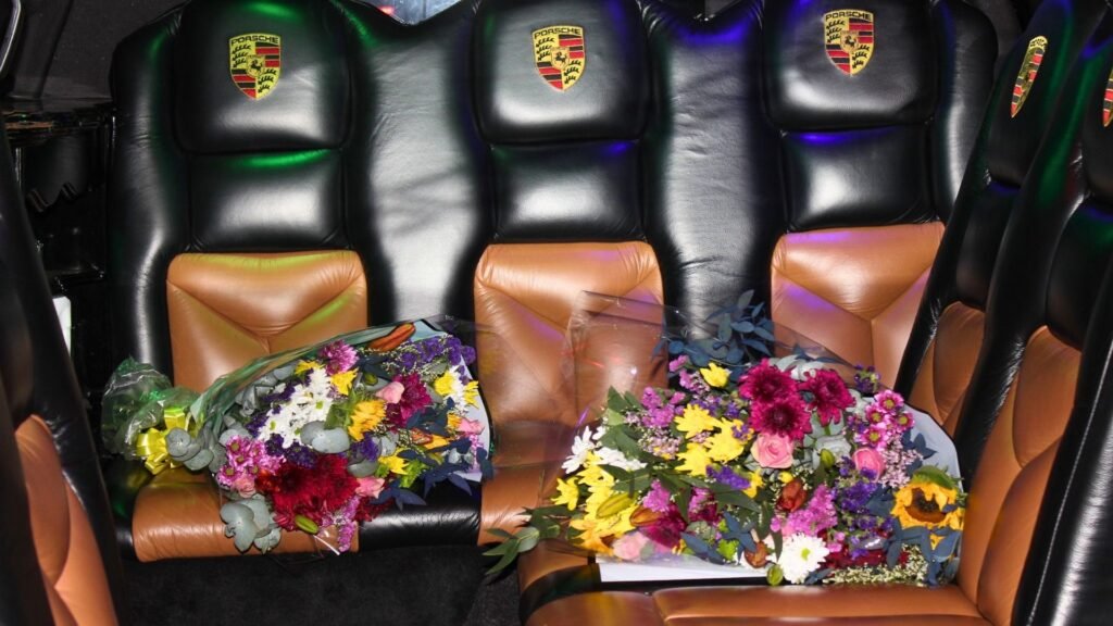 Two vibrant floral bouquets resting on tan and black Porsche-branded leather seats inside Luxury Limousines