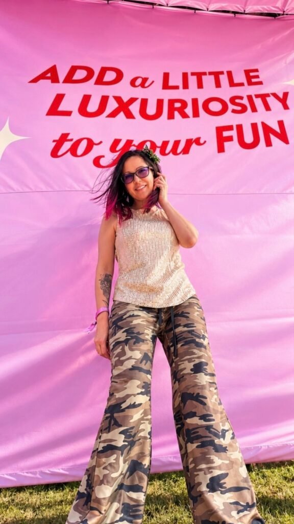 Claudia posing in front of a pink banner that reads "Add a little luxuriosity to your fun" at the event.