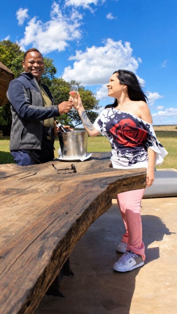 Claudia toasting champagne with private butler George at the wooden outdoor table of Sibani Lodge private villa