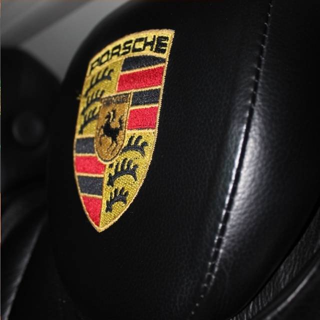 Close-up of the embroidered Porsche crest on black leather headrest inside Luxury Limousines stretch limousine