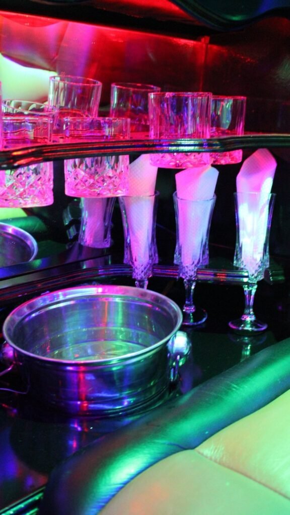 Close-up of crystal glasses, white napkins and silver ice bucket under pink and purple LED lighting in the Luxury Limousines bar