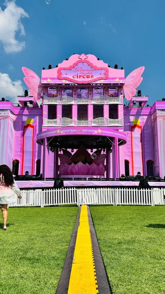 The grand pink festival stage featuring butterfly wings and a central lotus design under a blue sky at The Luxurious Marble Circus.