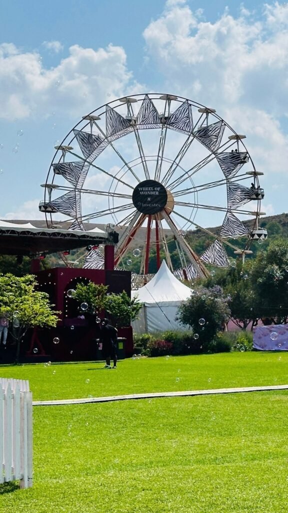 The Wheel of Wonder ferris wheel with zebra-patterned canopy accents set against a green lawn and blue sky at the Luxurious Marble Circus event.