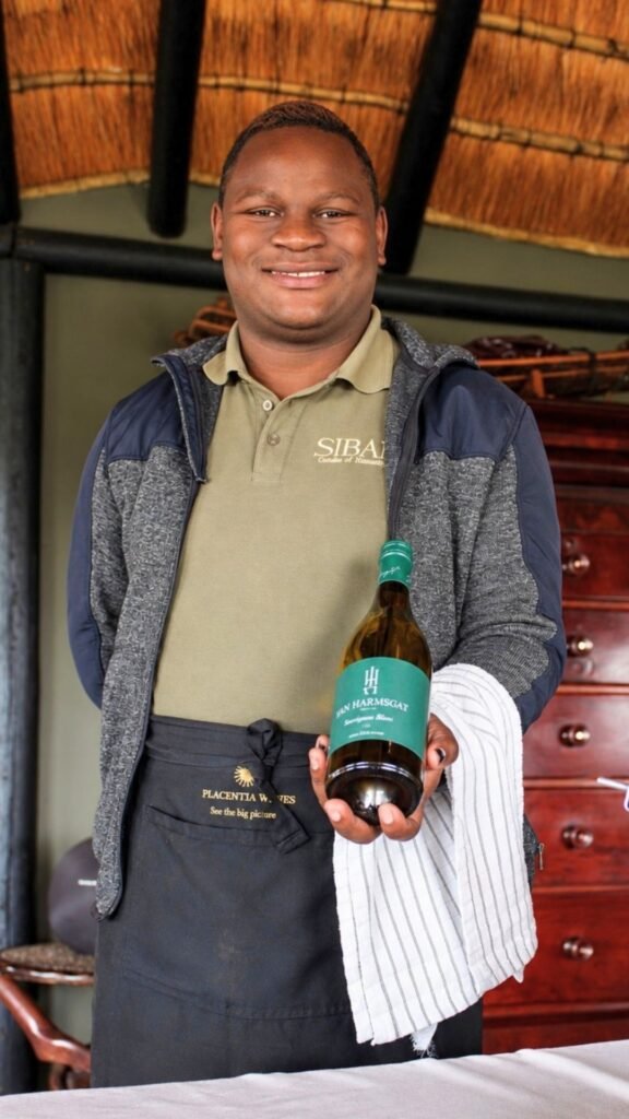 Friendly staff member presenting a bottle of Jan Harmsgat Sauvignon Blanc at Sibani Lodge