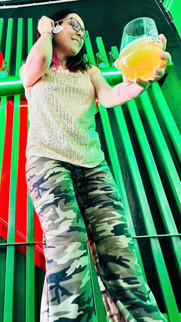 Claudia holding a branded Heineken Studio glass against a green slatted wall backdrop at the festival.