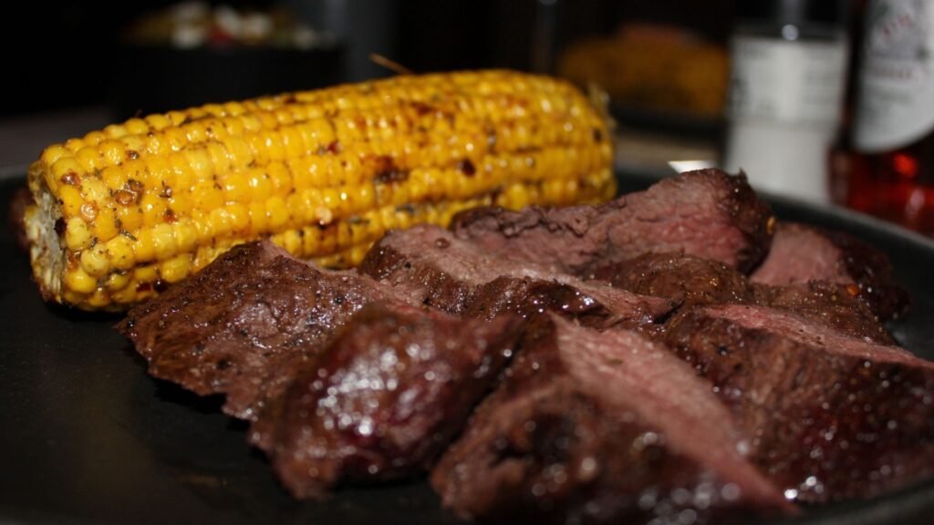Sliced medium-rare steak with grilled corn on the cob at Sibani Lodge