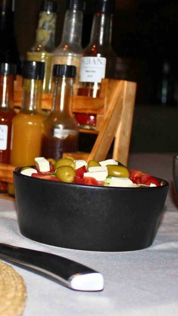Greek salad bowl next to a selection of Sibani Lodge house-made sauces