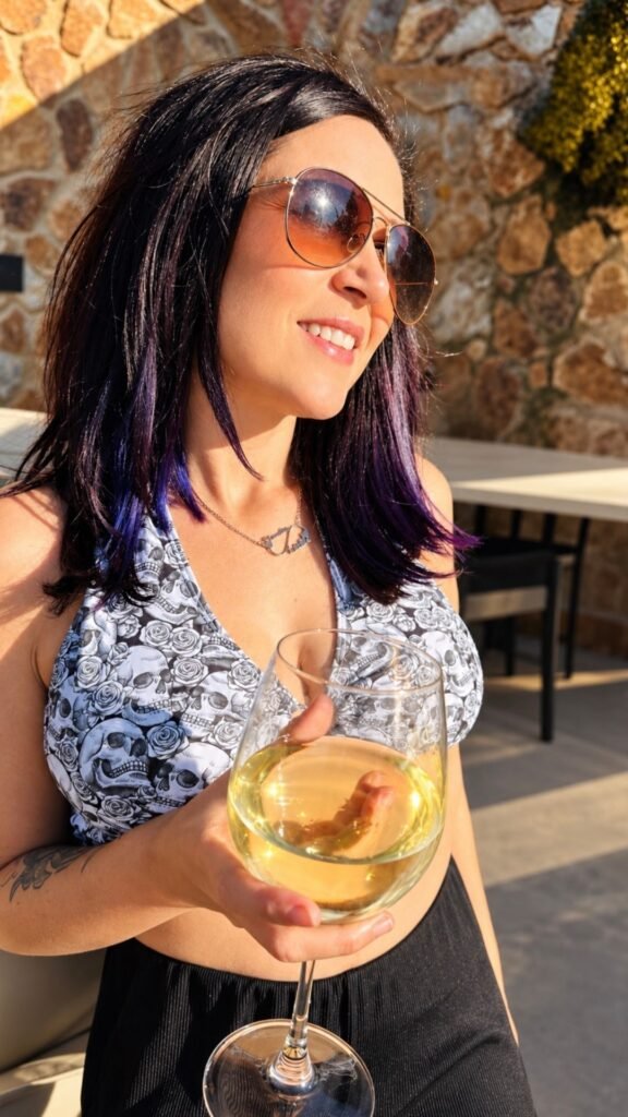 Claudia smiling with a glass of white wine in the outdoor area of Sibani Lodge