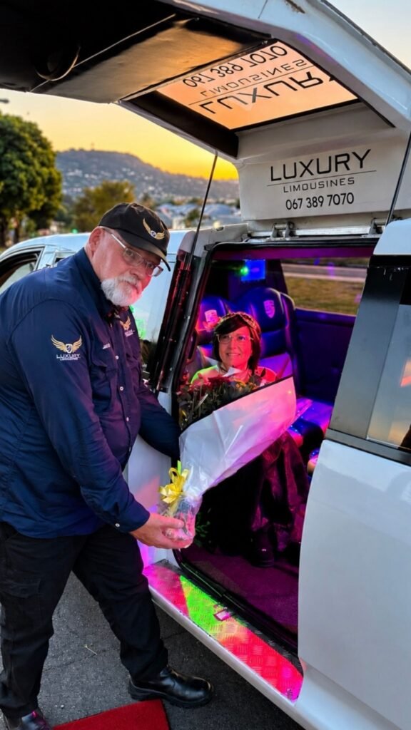 Chauffeur Jaco handing a large bouquet of flowers to Claudia Sherrin seated inside the Luxury Limousines Porsche Cayenne at sunset