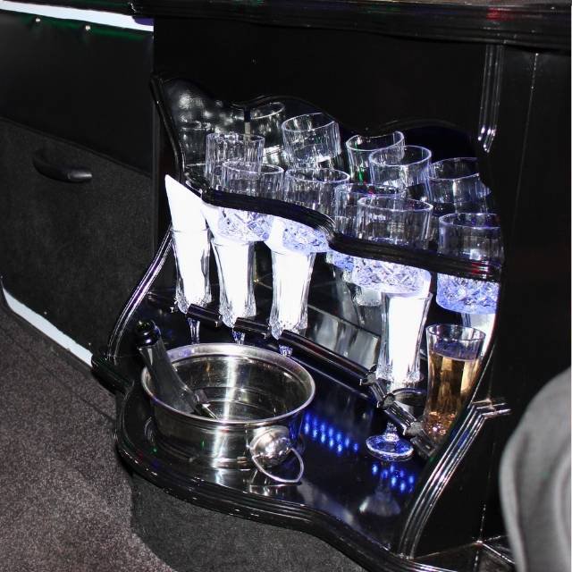 Crystal tumblers, champagne flutes and ice bucket on the mirrored bar shelf inside the Luxury Limousines stretch limo